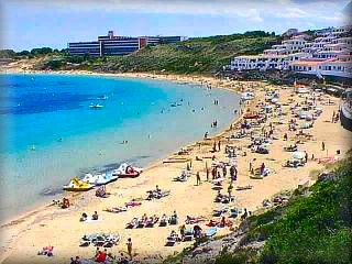 La playa de arenal de`n Castell es una aplia herradura, con muchos apartamentos turisticos y otros alojamientos sobre la misma arena de la playa al final hay un bosque de pinos