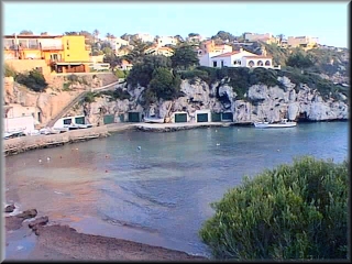 Vista de la playa de Cala Canutells, al fondo las casetas frente al embarcadero y el muelle sde las barcas de los pescadores y algun barco de recreo